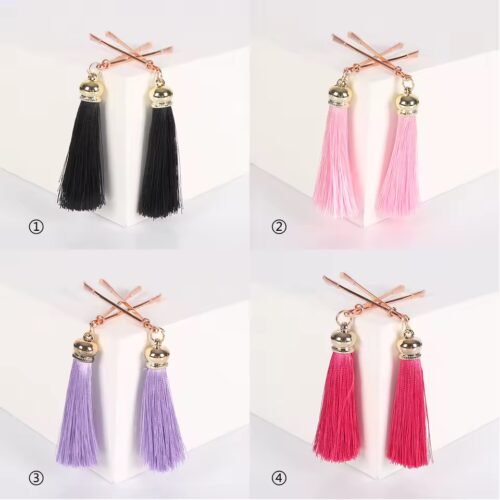 Pair of rose gold metal nipple clamps with black tassels on satin background
